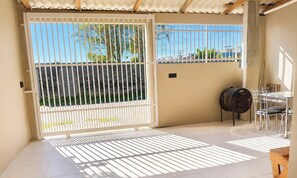 Eine überdachte Terrasse mit einem Metallzaun, einem Grill und einem Tisch mit Stühlen.
