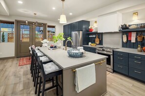 Une cuisine moderne dotée d’un îlot central, de meubles de rangement aux couleurs sombres, d’appareils électroménagers en acier inoxydable et offrant une vue sur l’extérieur.