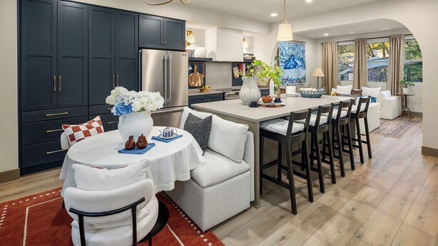 A modern kitchen with dark cabinets, a stainless steel refrigerator, and a dining area with a white table and chairs. - Delridge ArtHaus - Spacious 4-bedroom house in beautiful Seattle with AC (Seattle)