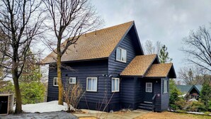 Una casa de dos pisos con exterior oscuro, techo inclinado y un pequeño porche frontal.