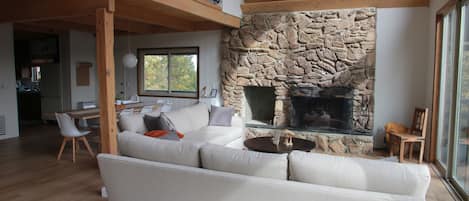 A spacious living area with a stone fireplace, a high ceiling with wooden beams, and a balcony.