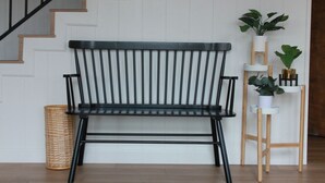 Una escalera de madera con barandal negro, un banco negro y un atril con plantas en macetas.