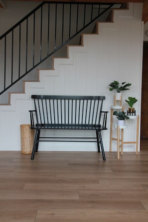 Uma escada de madeira com corrimão preto, um banco preto e um suporte de plantas com vasos.