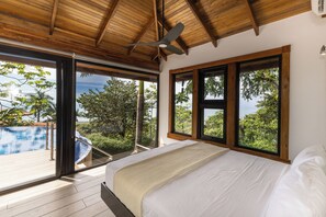 Un dormitorio con una cama grande, techo de madera y vistas a una piscina y follaje.