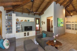 A spacious living room with a flat-screen TV, built-in shelves, and a wooden ceiling. - Casa Perezoso - Private Home w. Pool & Ocean View + Jungle Guest house (Escaleras)