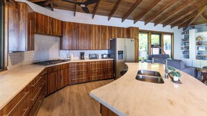 Eine moderne Küche mit Holzschränken, einer großen Kochinsel mit Spüle, einem Einbauofen und einem Kühlschrank.