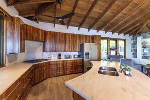 Eine moderne Küche mit Holzschränken, einer großen Kochinsel mit Spüle, einem Einbauofen und einem Kühlschrank.