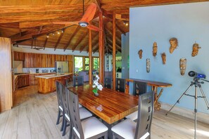A spacious kitchen with wooden cabinets and a central island, a dining area with a wooden table and chairs, and a ceiling fan. - Casa Perezoso - Private Home w. Pool & Ocean View + Jungle Guest house (Escaleras)