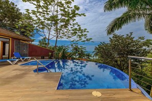 A swimming pool with a wooden deck, lounge chairs, and a view of the ocean. - Casa Perezoso - Private Home w. Pool & Ocean View + Jungle Guest house (Escaleras)
