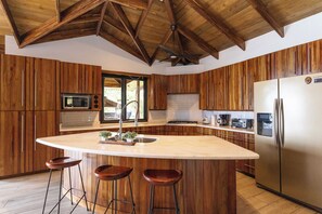Una cocina con armarios de madera, una isla central con taburetes, un refrigerador y un microondas.
