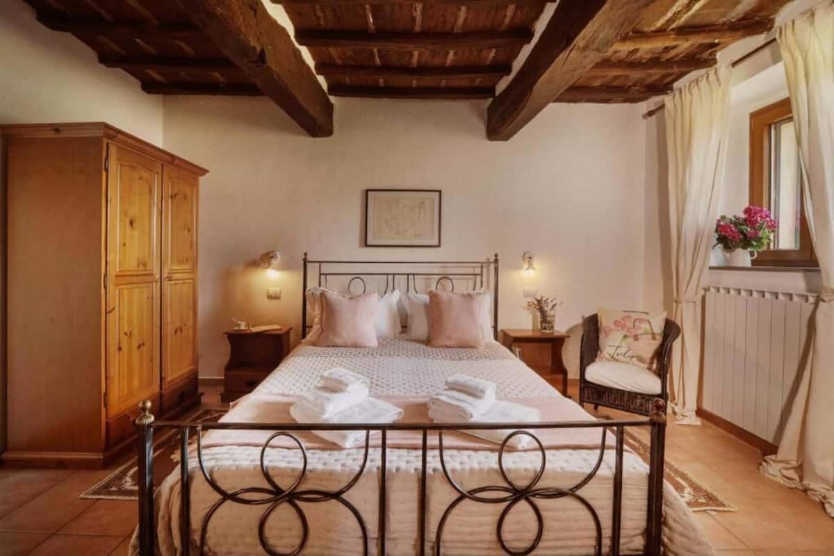 A bedroom with a bed, wooden wardrobe, bedside tables, a chair, and a window with curtains.