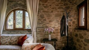 A stone-walled room with a sofa, a coat rack, and a window with curtains.