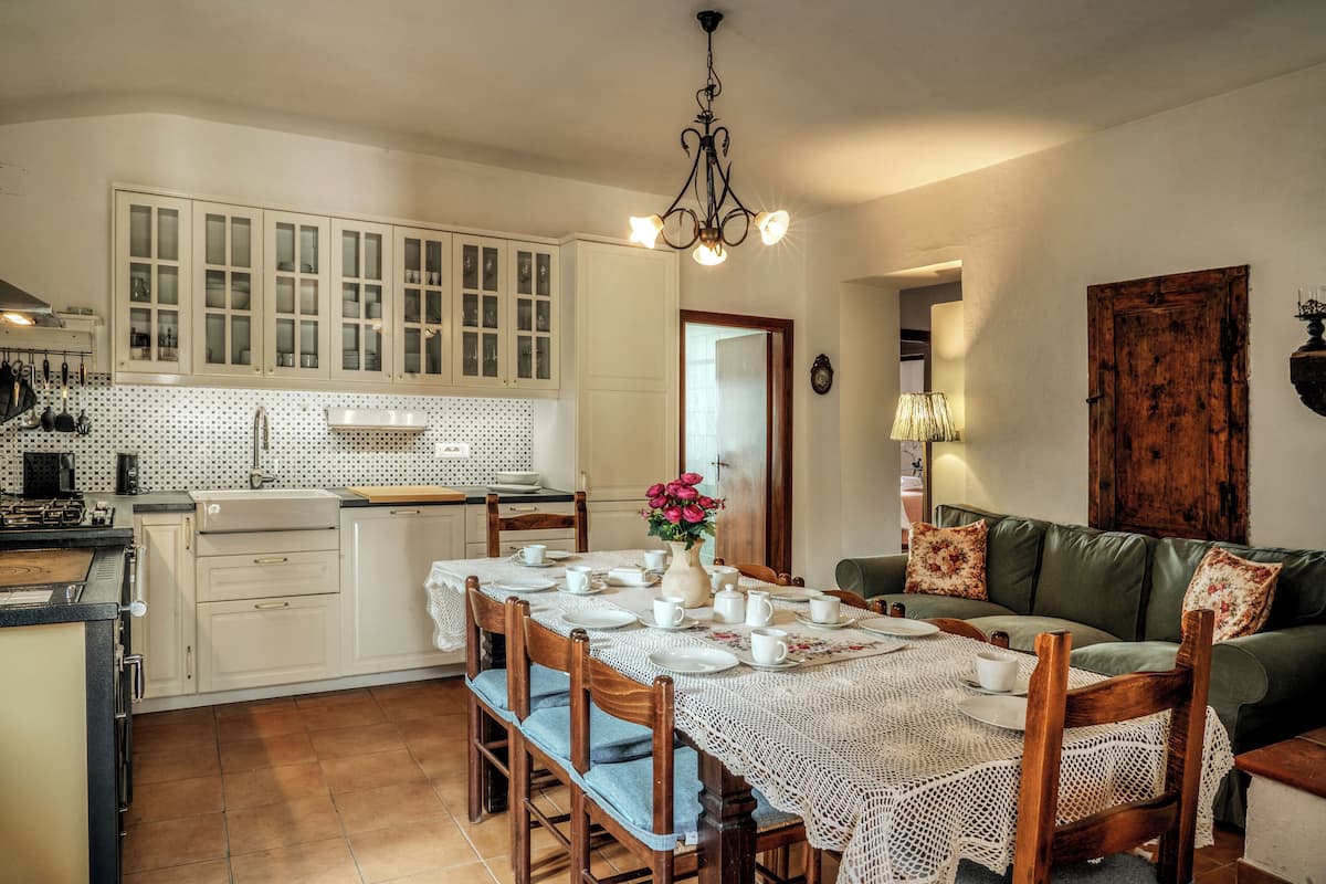 A kitchen with white cabinets, a dining table set for four, and a green sofa in the living area.