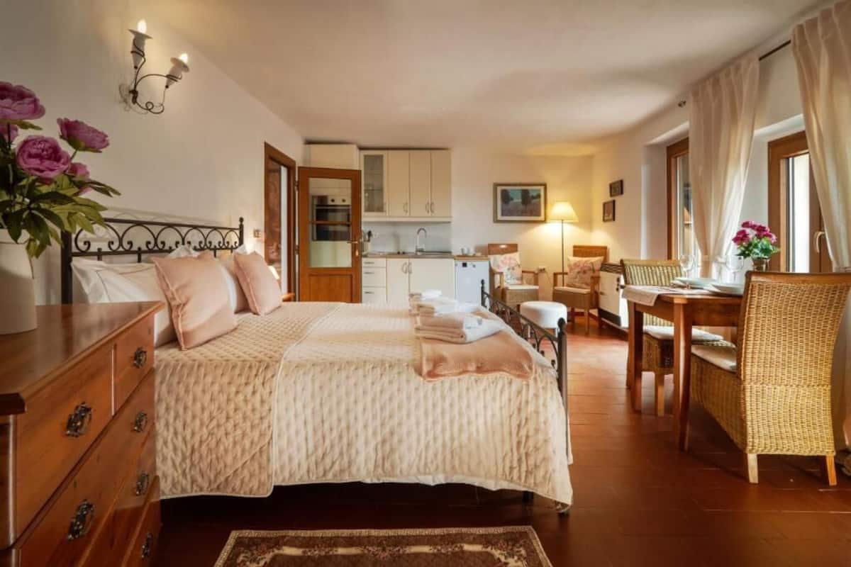 A bedroom with a bed, dresser, bedside table, and a view of the kitchen.