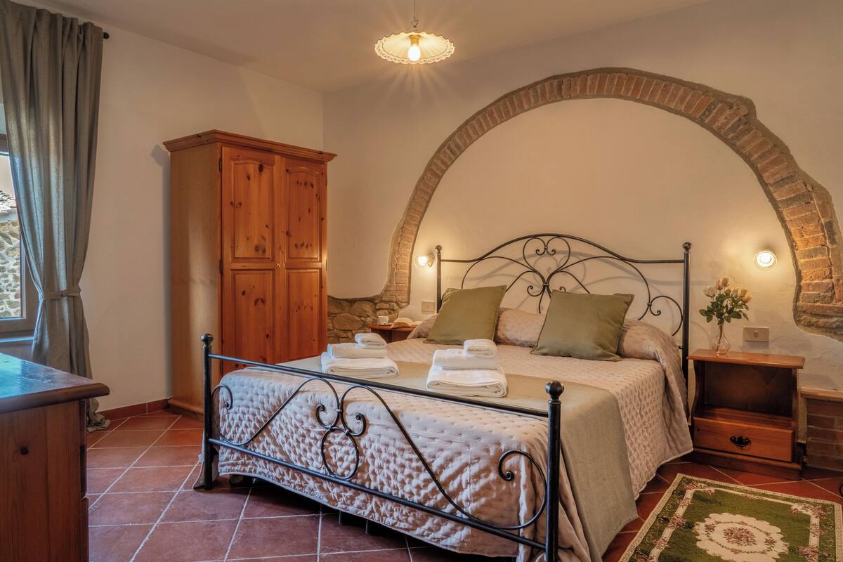 A bedroom with a bed, a wooden wardrobe, a stone wall, and a tiled floor.
