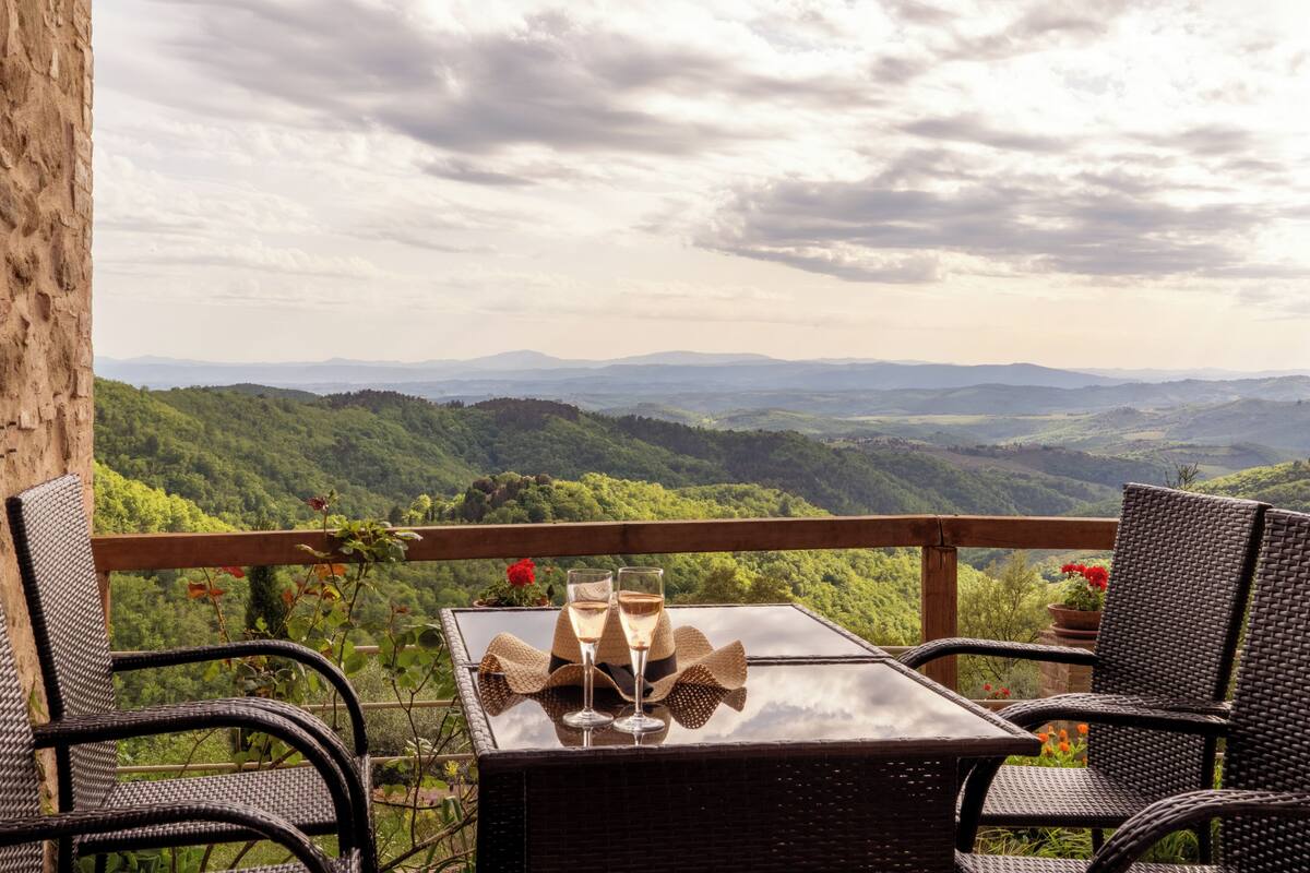 A balcony with wicker chairs and a table, overlooking a mountainous landscape.