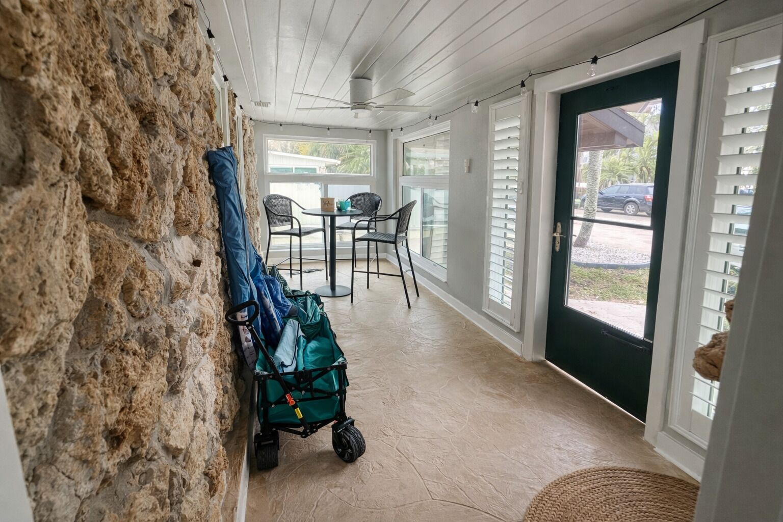 A covered porch with a stone wall, a green stroller, and a table with chairs.