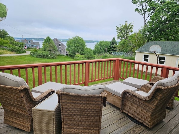 A deck with wicker furniture and a red railing overlooking a body of water.