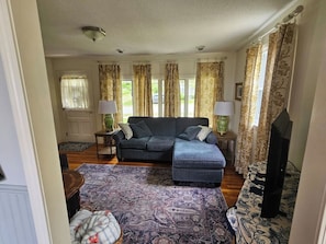 A living room with a sofa, ottoman, two lamps, a television, and patterned rugs.