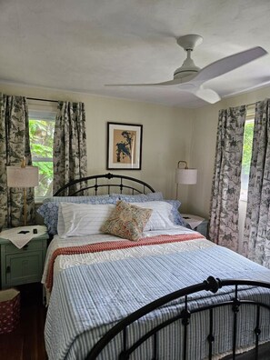 A bedroom with a bed, a ceiling fan, a nightstand, a lamp, and curtains.