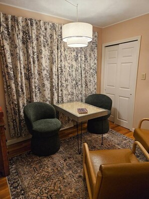 A room with a table, two chairs, a hanging light fixture, a patterned curtain, and a door.