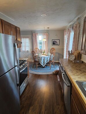 A kitchen with a central island, wooden cabinets, a stainless steel refrigerator, and a dining table with chairs. - Water Street Retreat (Eastport)