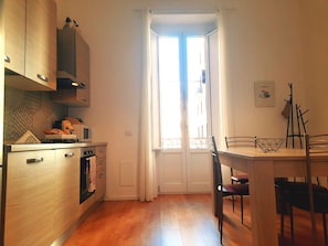 A kitchen with wooden cabinets, a microwave, and a dining area with a table and chairs. - Domus Velia Central Apt | Just Steps from the Station, Port, and Old Town (Salerno)