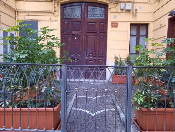 A courtyard with a dark wooden gate, potted plants, and a cobblestone path. - Domus Velia Central Apt | Just Steps from the Station, Port, and Old Town (Salerno)