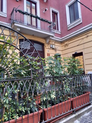 A building with a balcony, potted plants, and a door with a window. - Domus Velia Central Apt | Just Steps from the Station, Port, and Old Town (Salerno)