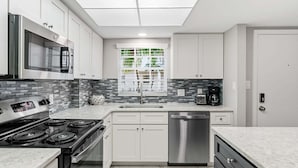 A modern kitchen with a built-in oven, microwave, and dishwasher, a window with a view of greenery, and a tiled backsplash. - Modern 2BR, 2BA condo in Sarasota's Palm Bay Club, sleeps 6 comfortably. (Sarasota)