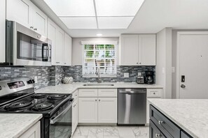 A modern kitchen with a built-in oven, microwave, and dishwasher, a window with a view of greenery, and a tiled backsplash. - Modern 2BR, 2BA condo in Sarasota's Palm Bay Club, sleeps 6 comfortably. (Sarasota)