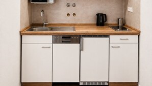 Una cocina compacta con armarios blancos, microondas, cafetera y lavavajillas.