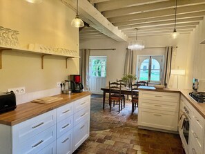 A kitchen with a coffee maker, a toaster, and a sink. There is a dining table with chairs and a vase with flowers. The room has a wooden ceiling and a window. - Les Bergeries across from a 16th-century manor house   (Saint-Germain-de-la-Coudre)
