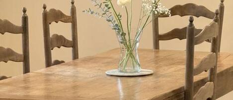 Une table à manger en bois sur laquelle est posé un vase en verre transparent contenant des fleurs blanches et des feuilles vertes.