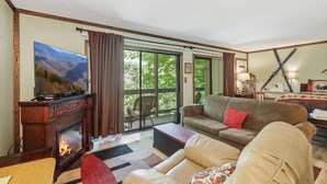 Ein Wohnzimmer mit Kamin, Fernseher, einer Couch und einem großen Fenster.