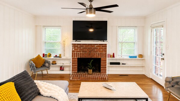 A living room with a fireplace, a television, and a ceiling fan.