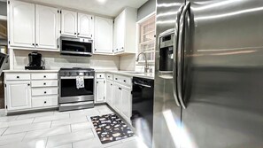 A modern kitchen with white cabinets, a stainless steel refrigerator, a microwave, an oven, and a dishwasher.