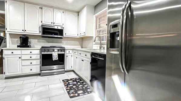 A modern kitchen with white cabinets, a stainless steel refrigerator, a microwave, an oven, and a dishwasher.