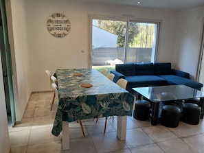 A dining area with a table and chairs, a sofa, and a glass coffee table. - APARTMENT NEAR THE BEACH WITH A GARDEN (Saint-Brevin-les-Pins)