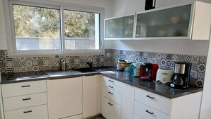 Een keuken met witte kasten, een zwart aanrecht, een raam en een betegelde achterwand met een patroon.
