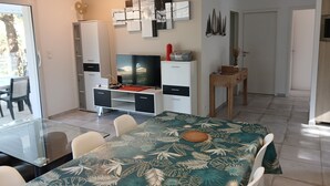 Een moderne woonkamer met een glazen eettafel, een flatscreen televisie en een wit kastje.