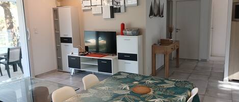 A modern living room with a glass dining table, a flat-screen TV, and a white cabinet.