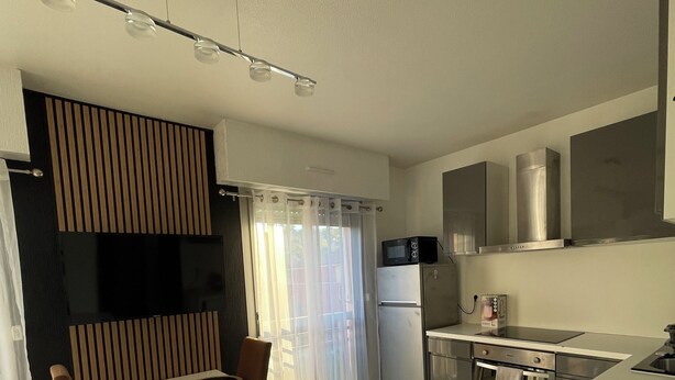A modern kitchen with a dining area, stainless steel appliances, and a flat-screen TV. - GOLFE-JUAN (06220) WEEKLY STUDIO RENTAL – JULY & AUGUST (Vallauris)
