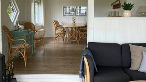 Ein großzügiger Wohnbereich mit einem dunklen Sofa, Holzboden und einem Essbereich mit Korbstühlen.