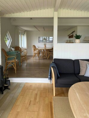 Ein großzügiger Wohnbereich mit einem dunklen Sofa, Holzboden und einem Essbereich mit Korbstühlen.