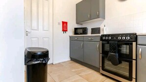 A kitchen with grey cabinets, a black oven, a microwave, and a trash bin. - House Sleeps 8 With Garden and Parking (Wolverhampton)