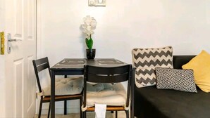 A dining area with a table, chairs, a potted orchid, and a black sofa with patterned cushions. - House Sleeps 8 With Garden and Parking (Wolverhampton)