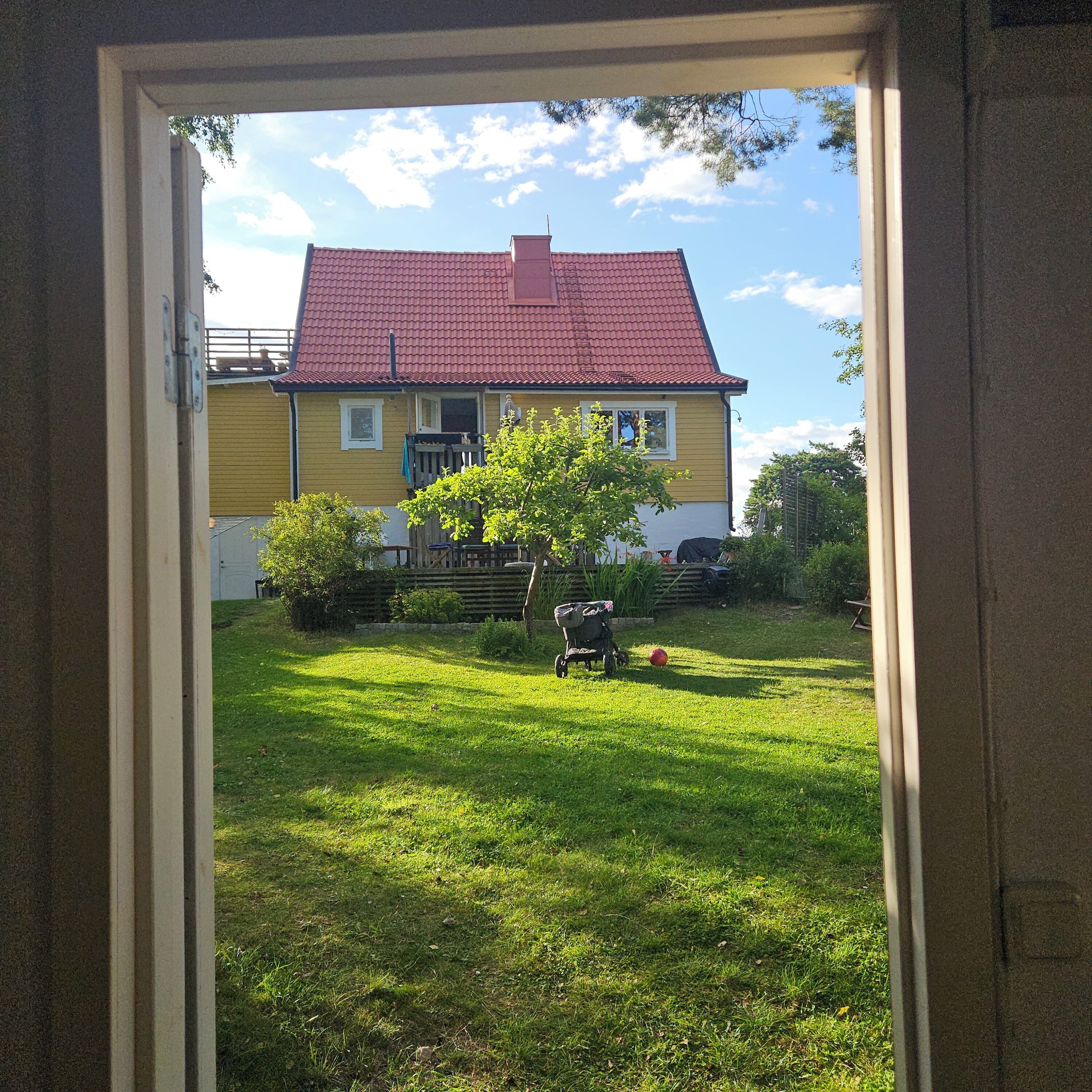 Een huis met een rood dak en een geel gevel, bezien door een geopende deur.