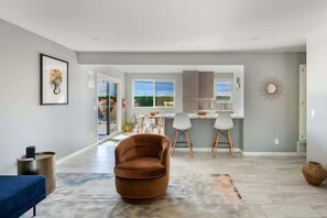 A spacious living area with a large brown chair, a dining table with chairs, and a kitchen in the background. - Salt & Sun Palm Springs by Navigate Stays (Palm Springs)