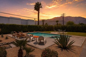 A pool area with lounge chairs, a table, and a mountain view at sunset. - Salt & Sun Palm Springs by Navigate Stays (Palm Springs)